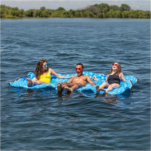 Three people on a blue inflatable raft in a lake with trees in the background