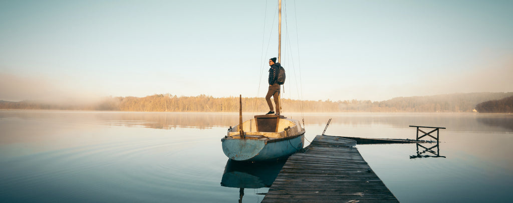 Person standing on wooden sailboat at dock on a hazy day with a calm lake.