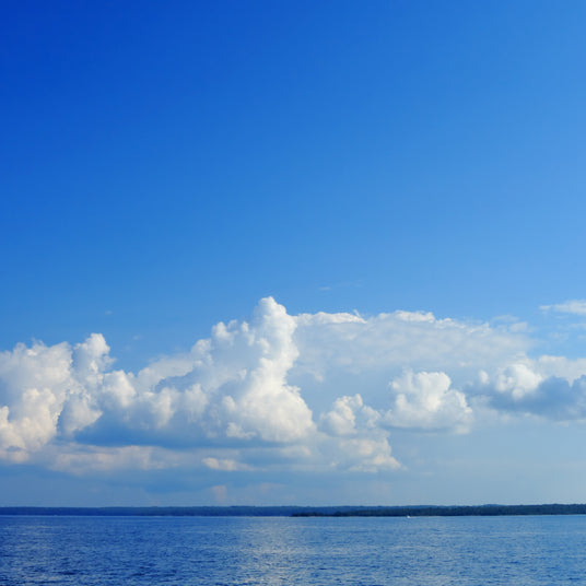 Blue sky with fluffy white clouds over a calm body of water
