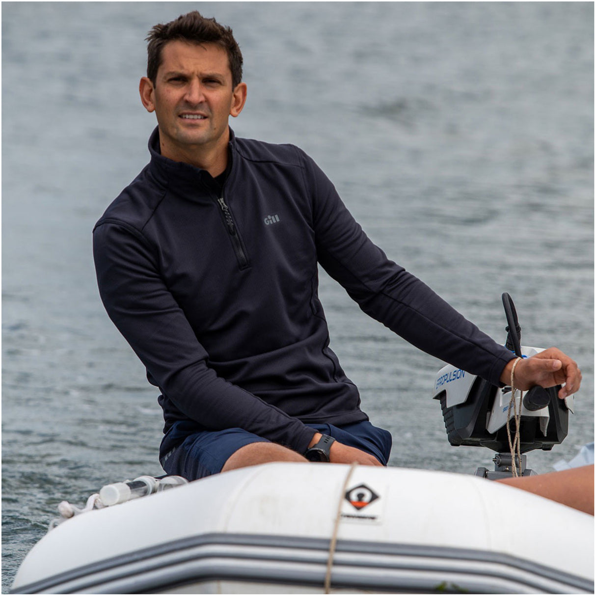 Man sitting on a boat wearing a dark blue jacket with water in the background