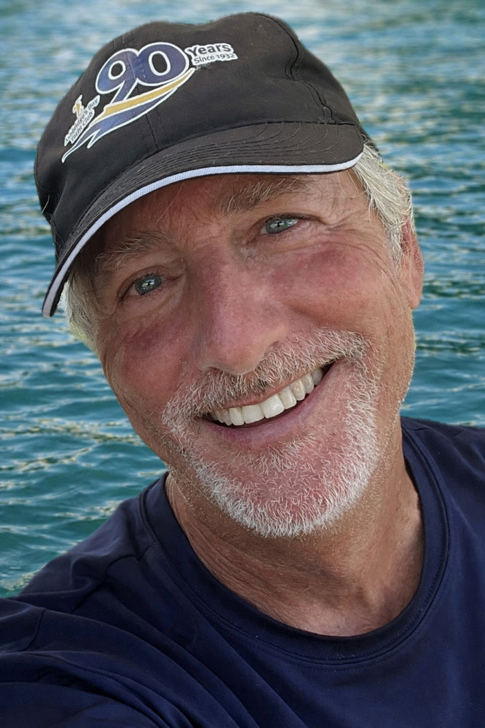Man wearing a cap with '90 Years' text, smiling in front of water.