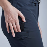 Person wearing dark pants with a hand in a pocket holding a black object against a light gray background