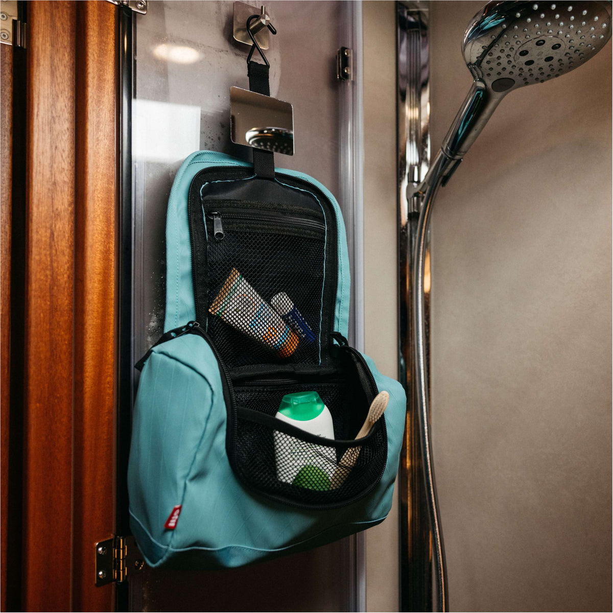 A light blue and black shower wall bag hanging on a shower door in a bathroom, filled with toiletries.