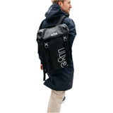 A man wearing a dark navy hooded jacket and beige pants, shown from the side/back, carrying a black Gill pack with white branding on a plain white background.