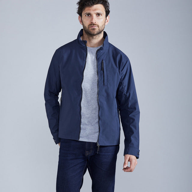 Man wearing a navy blue jacket over a gray shirt on a light gray background