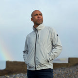 Man wearing a light gray jacket standing on a beach with a rainbow in the background