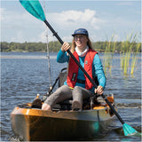 Person kayaking on a lake with a fishing rod and life jacket.