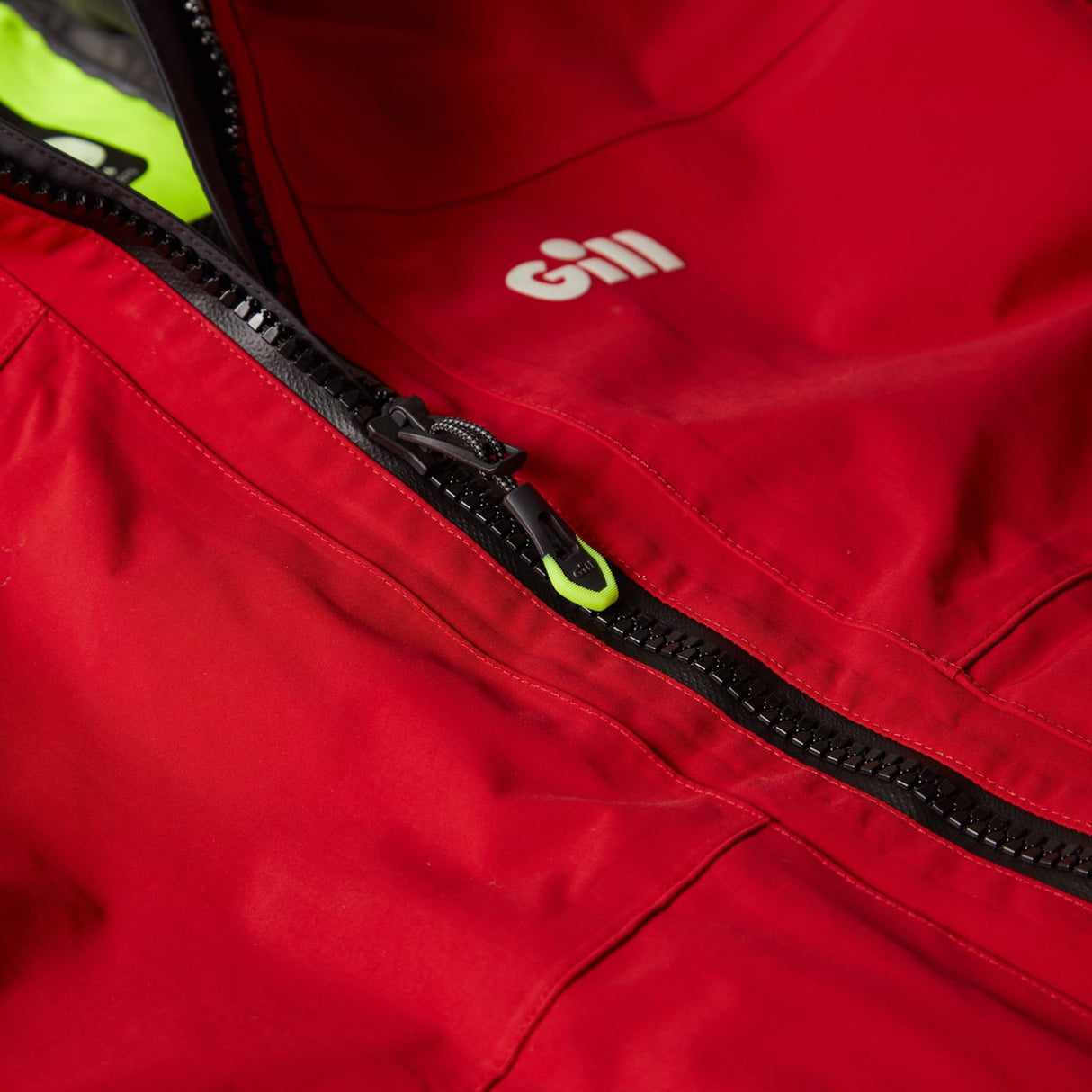 Close-up of a red jacket with a zipper, featuring the Gill brand logo.
